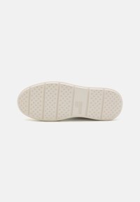 White rubber outsole with textured grip pattern, featuring horizontal ridges and a prominent logo embossed on the side.