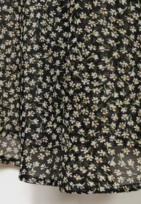 Tissu noir avec un motif floral comportant des fleurs blanches et des tiges vertes, créant une texture délicate. Le design est léger et transparent.