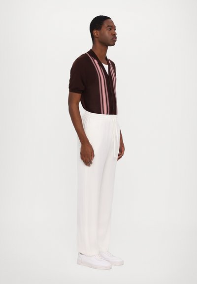 Brown short-sleeve shirt with pink stripes, paired with white elastic-waist trousers and white sneakers. Simple design, relaxed fit.