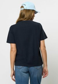 Temno modra bombažna majica s kratkimi rokavi, okroglim izrezom in sproščenim krojem, v kombinaciji z visokimi modrimi kavbojkami in svetlomodro kapo.