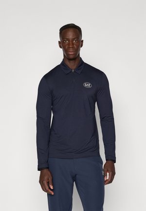Polo shirt à manches longues bleu marine avec un col zippé, tissu texturé et logo EA7 sur la poitrine. Assorti à un pantalon sombre, coupe ajustée.