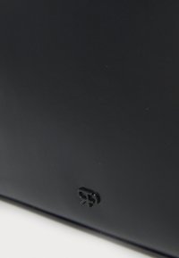 Surface noire avec un petit logo en relief brillant près du bord inférieur sur un fond mat lisse.