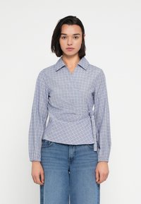 Καρό πουκάμισο τύπου wrap σε ανοιχτό γαλάζιο και λευκό, μακριά μανίκια, με γιακά, διακοσμημένο με δέσιμο στο πλάι, σε συνδυασμό με ψηλόμεσα τζιν παντελόνια.