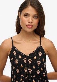Vestido negro sin mangas con un patrón floral en rosa y verde, que presenta un escote en V y botones decorativos en la parte delantera.