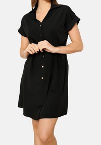 Czarna sukienka koszulowa z gładkiej tkaniny, z kołnierzykiem, krótkimi podwiniętymi rękawami oraz przewiązanym paskiem w talii, ozdobiona złotymi guzikami z przodu.