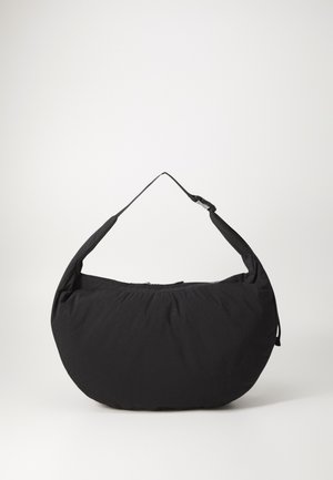 Bolsa de ombro de tecido preto com uma forma curvada, com uma alça única e fecho com zíper. Textura suave, design minimalista.