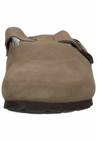 Zapato marrón de ante sin cordones con punta redondeada, una sola correa ajustable y una suela baja texturizada. Forro interior suave visible.