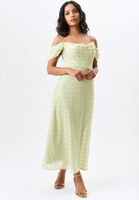 Light green dress with off-the-shoulder sleeves, polka dot pattern in gold, flowing fabric, knee-length, paired with gold strappy heels.
