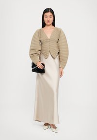 Beige, ribbed crop top with long, puffed sleeves and buttons. Flowing, cream satin maxi dress. Black handbag with chain strap. Pointed beige heels.
