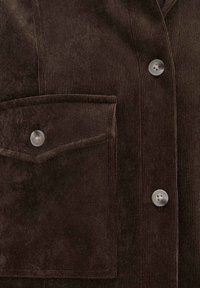 Veste en velours côtelé marron foncé devant montrant une poche à rabat avec bouton et deux boutons visibles le long de la patte de boutonnage.