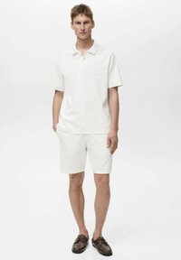 Chemise polo blanche et shorts assortis, en tissu lisse, avec un col classique et des manches courtes, accompagnés de chaussures marron.