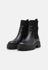 Botas de tobillo negras con textura de cocodrilo, parte superior de ribete elástico y suela gruesa y resistente. Incluye tiradores para facilitar el uso.
