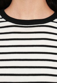 Πλεκτό ύφασμα με ασπρόμαυρες ρίγες και ριμπ ύφανση σε μαύρο λαιμόκοψη. Οι ρίγες είναι ομοιόμορφα κατανεμημένες, δημιουργώντας ένα κλασικό οριζόντιο σχέδιο.