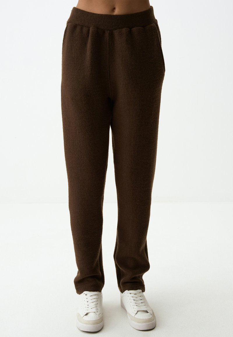 Braune Fleece-Jogginghosen mit elastischem Bund und Seitentaschen, mit einer weichen Textur und einer lässigen Passform, kombiniert mit weißen Sneakers.