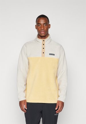 Lys beige og gul fleece genser med ståkrage, knappestolpe og logomerke på brystet. Myk tekstur med et varmt utseende.