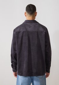 Chemise en velours côtelé gris foncé à manches longues, avec des côtes verticales, un col, et des poignets à boutons. Vue arrière affichée.