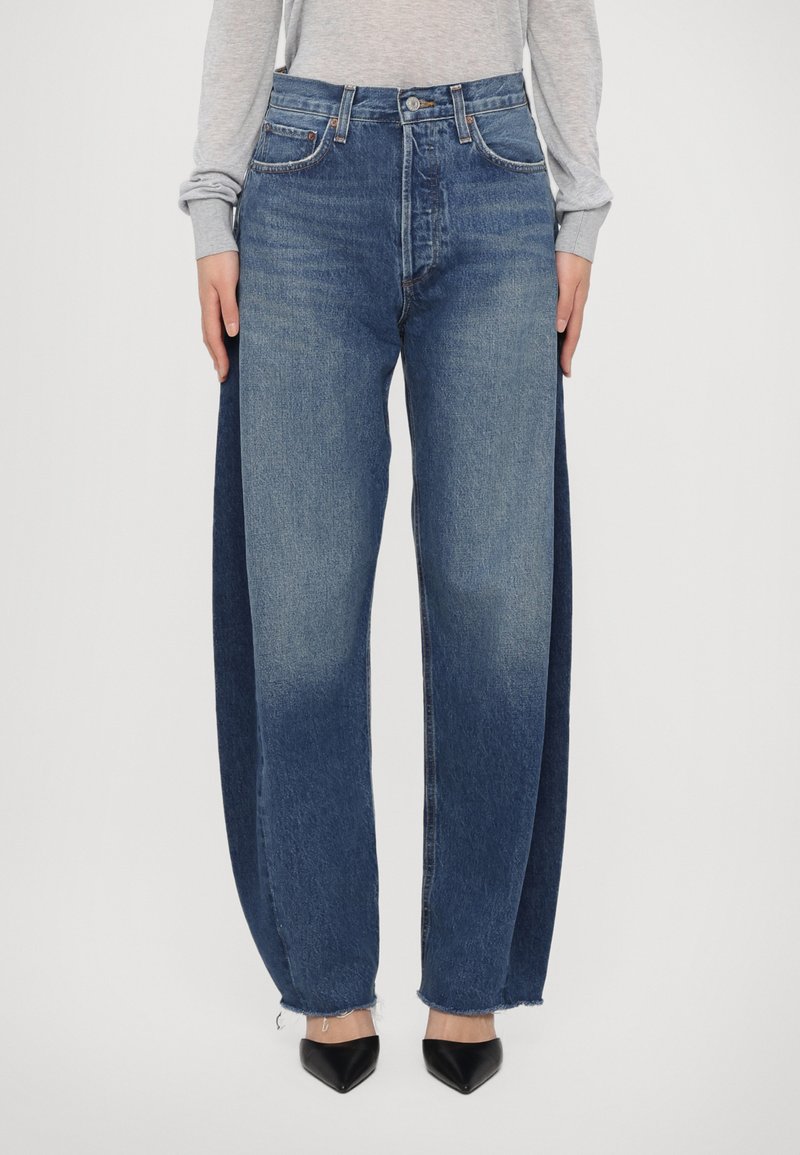 Laiad denim püksid kahetoonilise disainiga; esipaneel on heledam ja külgpaneelid tumedamad. Kulunud ääred ja traditsiooniline viie tasku stiil.