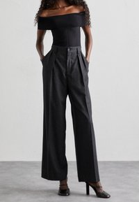 Top nero con scollo a spalle scoperte e texture a coste abbinato a pantaloni grigi a vita alta e gamba ampia con pieghe e tasche laterali.