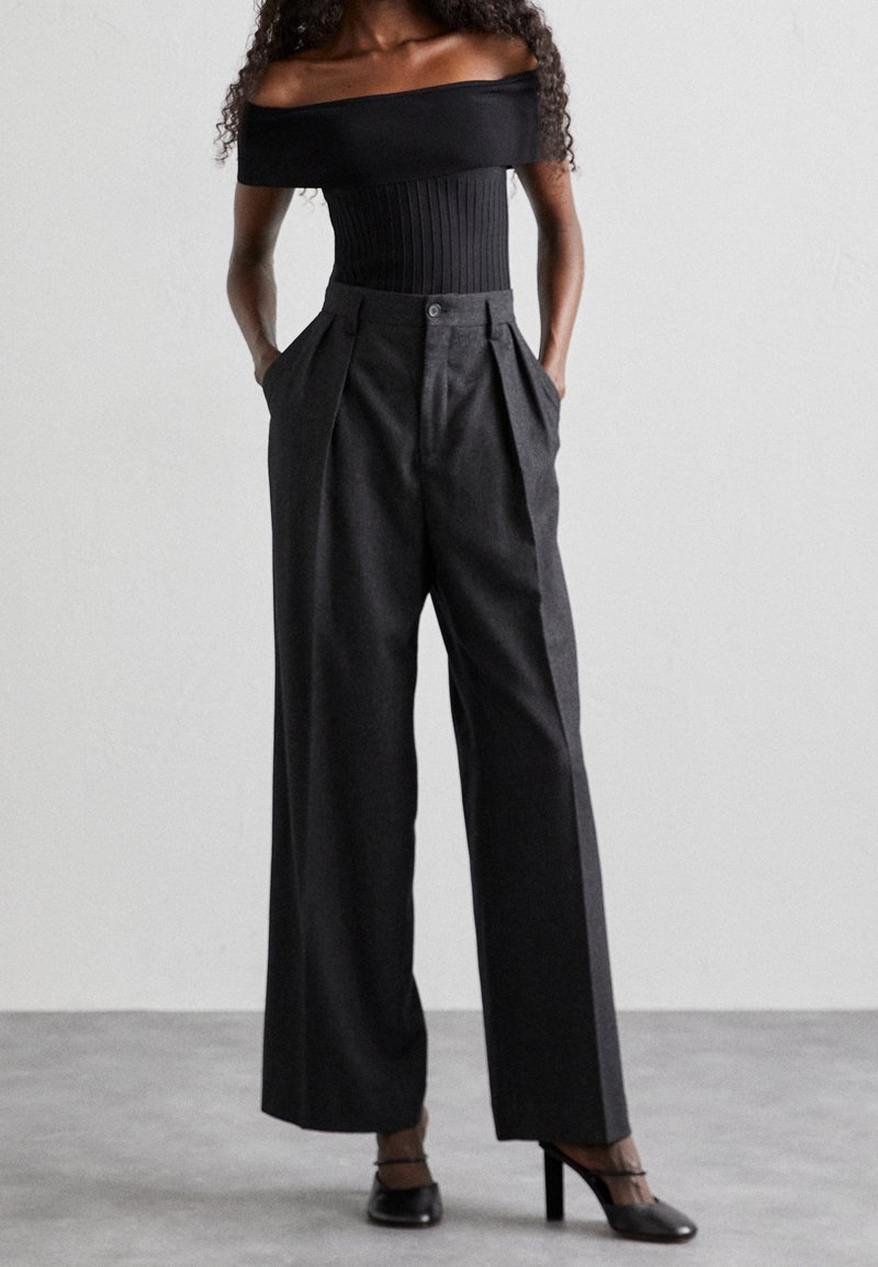 Top nero con scollo a spalle scoperte e texture a coste abbinato a pantaloni grigi a vita alta e gamba ampia con pieghe e tasche laterali.