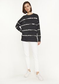Felpa nera con strisce bianche orizzontali, design rilassato, maniche lunghe, scollo tondo, abbinata a pantaloni bianchi slim-fit e sneakers bianche.