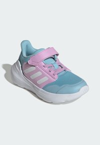 Jasnoniebieski but sportowy z różowymi akcentami, siateczkową cholewką, paskiem na rzep i białą śródstopą. Charakterystyczny detal z trzema paskami po bokach.