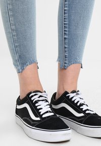 Zapatillas negras de ante con rayas laterales y cordones blancos. Llevadas con jeans azul claros que tienen los bajos deshilachados en los tobillos.