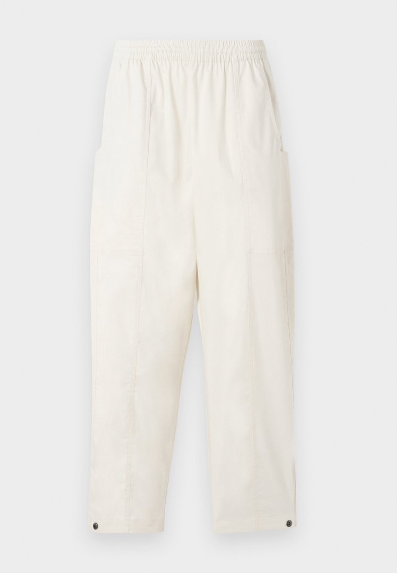 Pantalons beige clair, amples, avec une taille élastique, des poches latérales et des accents de boutons aux ourlets. Texture de tissu lisse.