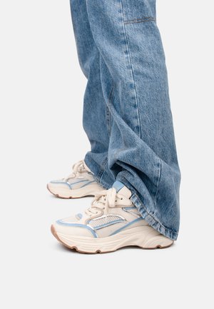 Chunky witte sneakers met blauwe accenten en netpanelen, gecombineerd met losse blauwe denim jeans met een vervaagde textuur en zichtbare stiksels.