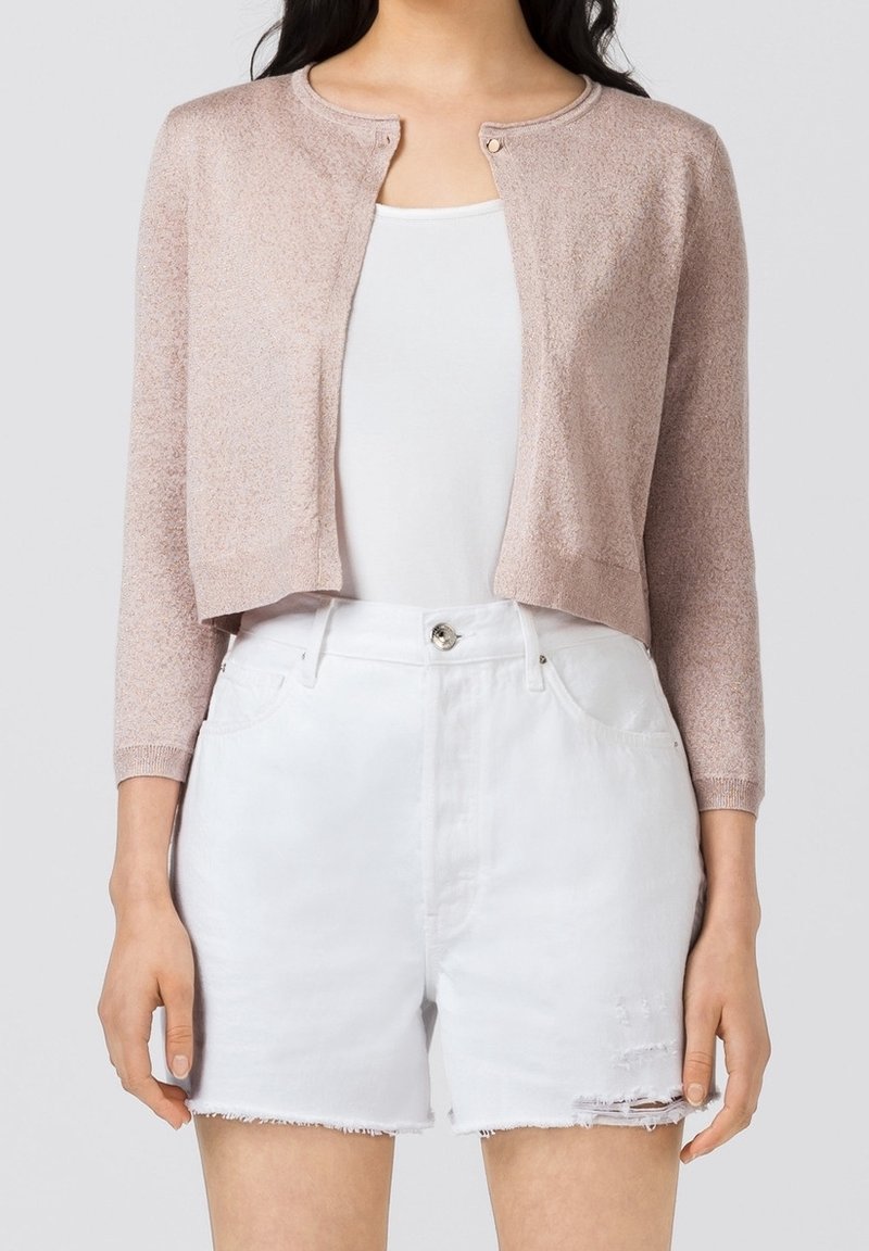 Cardigan rosa corto in maglia con colletto rotondo, maniche lunghe e un bottone davanti, abbinato a pantaloni corti in denim bianco con effetti distressed.