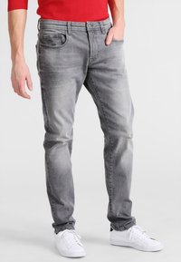Jeans de denim gris con un corte ajustado, que presentan bolsillos delanteros y un leve desvanecimiento. Combinados con zapatillas blancas para un estilo casual.