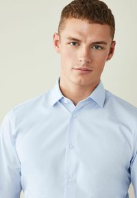 Hellblaues Button-Up-Hemd mit Kragen, aus einem glatten Stoff. Verfügt über ein tailliertes Design und sichtbare Knöpfe an der Vorderseite.