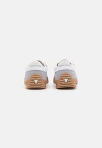 Pár šedých a bílých tenisek Converse s béžovými podrážkami a hvězdicovým logem na patě, zobrazené zezadu na bílém pozadí.