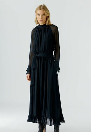 Schwarzes, langärmeliges Kleid aus leichtem Stoff. Mit hohem Kragen, gerafftem Oberteil und gerafftem Saum, der mit einem passenden Gürtel betont wird.