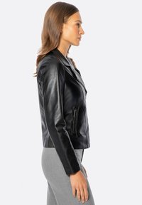 Chaqueta de motocicleta de cuero negro con un bolsillo con cremallera, cuello con muesca y un diseño ajustado. Modelo mostrado en vista de perfil.