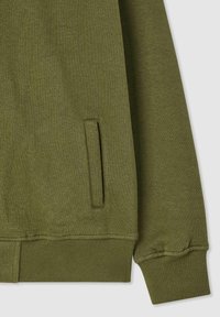 Felpa verde oliva con polsini e orlo a costine. Presenta una tasca laterale con un'apertura rettangolare, realizzata in morbido cotone.