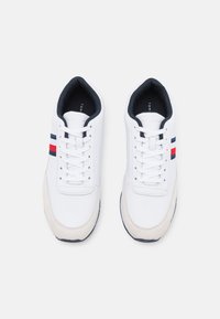 Scarpe da ginnastica bianche con strisce blu scuro e rosse, caratterizzate da una tomaia in pelle liscia e un cappuccio in suede beige chiaro. Design con lacci.