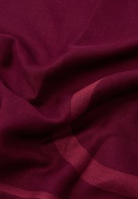 Dyb burgunder stof med glatte folder og subtile stribemønstre, der skaber bløde skygger og tekstur.