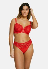 Bralette en dentelle rouge avec armatures et bretelles réglables, associé à une culotte assortie ornée de dentelle présentant un motif floral et un accent décoratif.