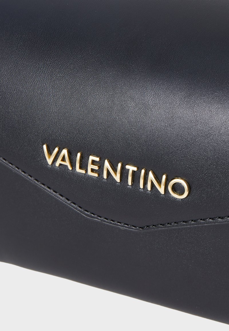 Sac à main en cuir noir avec un logo doré "VALENTINO", texture lisse et subtil détail de couture le long du bord.