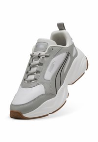 Sneaker grigio e bianco realizzato in materiali in pelle e rete, con suola spessa, punta arrotondata e logo Puma ben visibile sul lato.