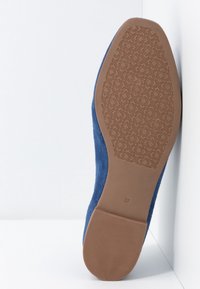 Chaussure plate en daim bleu avec une semelle en caoutchouc marron présentant une texture à motifs et une étiquette indiquant la taille 37. Vue de profil latérale.