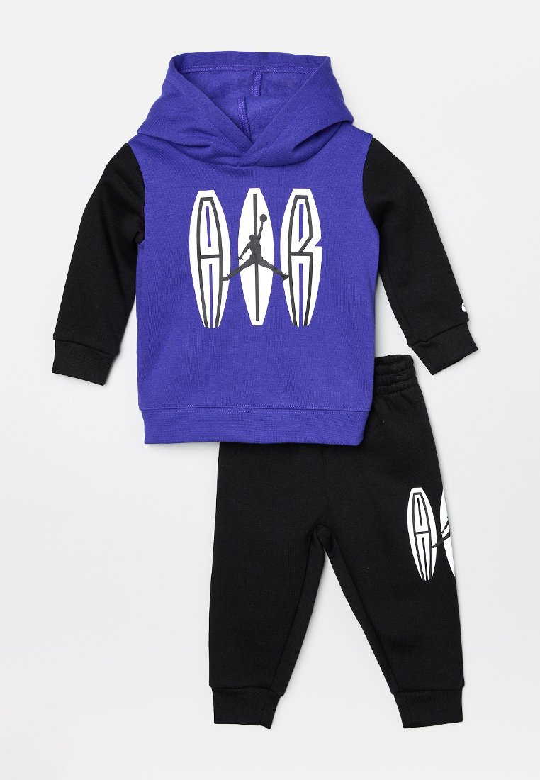 Conjunto de sudadera púrpura y negra que incluye capucha, logo gráfico y pantalones negros a juego con detalle del logo en la pierna. Tejido de mezcla de algodón.