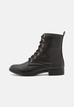 Czarny skórzany botek sięgający kostki z złotymi oczkami, czarnymi sznurówkami, niskim obcasem i pętelką z tyłu, prezentowany w profilu bocznym na białym tle.