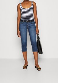 Canotta a righe blu navy e bianche con bottoni, abbinata a jeans blu a vita alta e sandali neri con tacco a blocco, mentre tiene una borsa tote nera.