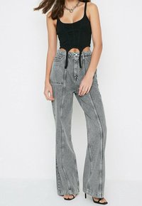 Top court noir avec détail texturé, associé à un jean large taille haute gris clair avec des coutures verticales et une taille à cordon.