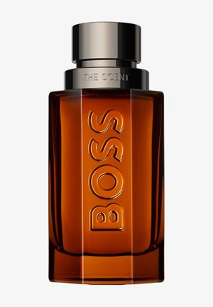 Flacon de parfum rectangulaire ambré avec "BOSS" embossé verticalement et un bouchon métallique portant l'inscription "THE SCENT" sur le dessus.