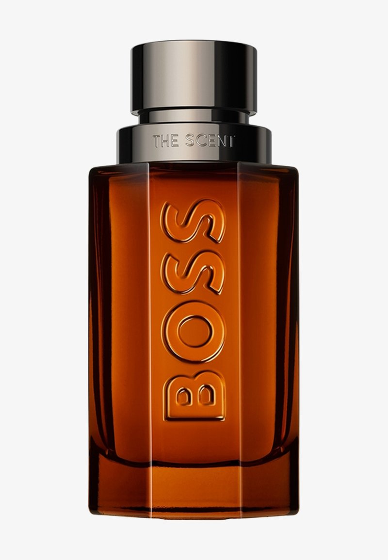 Flacon de parfum rectangulaire ambré avec "BOSS" embossé verticalement et un bouchon métallique portant l'inscription "THE SCENT" sur le dessus.