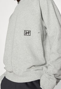 Grauer Sweatshirt aus Baumwollmischung mit gerippten Bündchen und Saum. Auf der Vorderseite befindet sich ein schwarzes rechteckiges Nike-Logo-Patch.