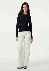 Must mustaheline topp, millel on ribitud tekstuur ja laineline äär, paaritatud valgete laiade pükste ja musta-valge triibuliste kingadega.