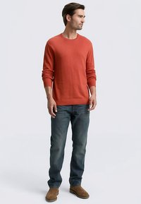 Maglione rosso a maniche lunghe con scollo a giro realizzato in tessuto morbido, abbinato a jeans blu scuro e stivaletti beige. Design semplice e aderente.